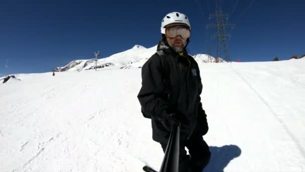 Широкоугольный лыжник-селфи в черном снаряжении и в белом шлеме едет на снежном склоне в солнечный день. Концепция зимних лыжных видов спорта — стоковое видео