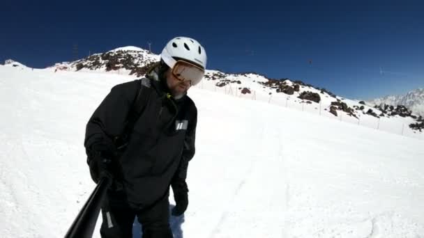 Siyah ekipman ve beyaz kask yaşlı bir selfie geniş açılı erkek kayakçı güneşli bir günde karlı bir yamaç üzerinde sürmek. Kış kayak sporları kavramı — Stok video