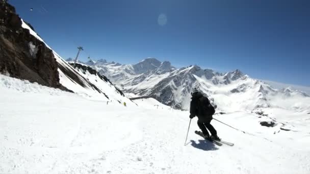 Широкоугольный лыжник в черном снаряжении и белый шлем с лыжными палками катается на снежном склоне в солнечный день. Концепция зимних лыжных видов спорта — стоковое видео