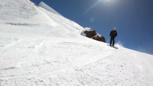 En vidvinkel manliga skidåkare åldrad i svart utrustning och vit hjälm med skidstavar rider på en snöig sluttning på en solig dag. Begreppet vinter skidsport — Stockvideo