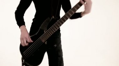 Beyaz arka planda siyah bas gitar ile siyah giysiler içinde genç erkek müzisyen. Bas gitarist anlamlı müzik oyunu