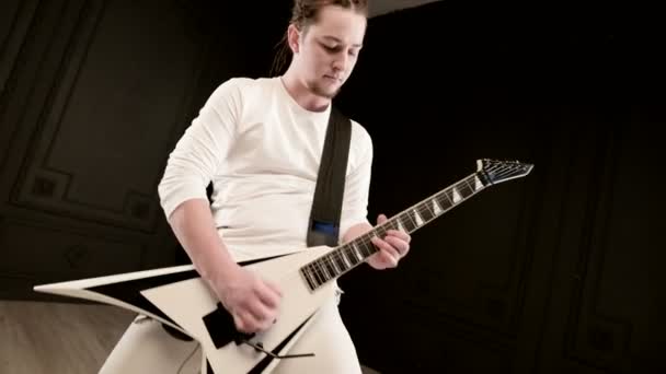 Стильный сольный гитарист с дредами на голове и в белой одежде на черном фоне, выразительно играющий на белой гитаре в черной студии — стоковое видео