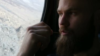 Arka koltukta arabada oturan ve dağların arka planına karşı yanlarda meditasyon konuşan sakallı bir hipster erkek yakın çekim portre