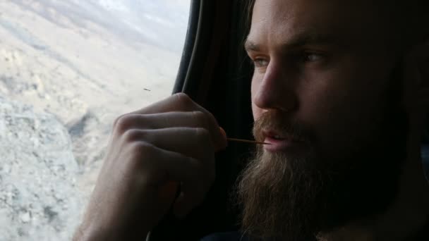 Közelkép portréja a beszélő szakállas csípő férfi ül az autóban a hátsó ülésen, és meditál az oldalán a háttérben a hegyek — Stock videók