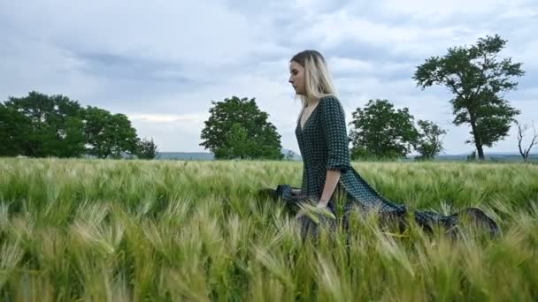 Genç mutlu sarışın kız yağmur gökyüzünün arka plan karşı akşam yeşil bir buğday tarlasında çalışır. Yan görünüm — Stok video