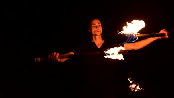 Low key. Young male with long hair and bare torso rotates burning torch outdoors on a black night video slow motion. Modern fakir does tricks with a burning staff — Stock Video