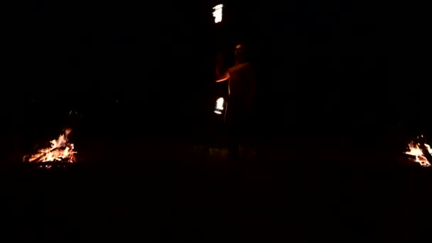 Niski klucz. Młody mężczyzna z długimi włosami i nagi tułowia obraca płonącego palnika na zewnątrz na czarno-noc wideo powolny ruch w pobliżu pożarów. Nowoczesny fakir robi sztuczki z płonącego personelu — Wideo stockowe
