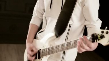 Siyah bir arka plan üzerinde beyaz giysiler içinde farklı gözleri ile Close-up Şık ritim gitarist ifade siyah bir stüdyoda beyaz gitar çalıyor