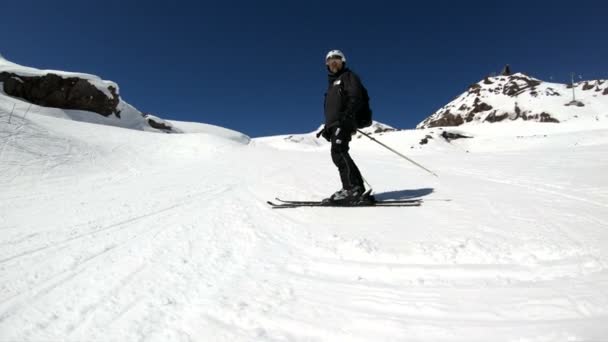 Siyah ekipman ve kayak direkleri ile beyaz kask yaşlı geniş açılı erkek kayakçı güneşli bir günde karlı bir yamaç üzerinde sürmek. Kış kayak sporları kavramı — Stok video