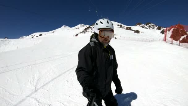 Ein Selfie-Weitwinkelskiläufer in schwarzer Ausrüstung und weißem Helm fährt an einem sonnigen Tag auf einem schneebedeckten Hang. das Konzept des Wintersports — Stockvideo