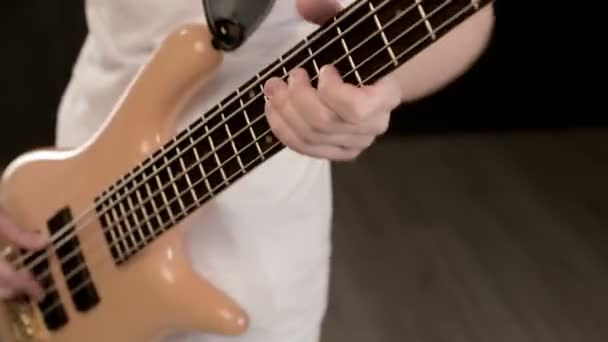 Junger männlicher Musiker in weißer Kleidung mit beiger Bassgitarre auf schwarzem Hintergrund. Bassist Gitarrist ausdrucksstarke Musik Spiel — Stockvideo