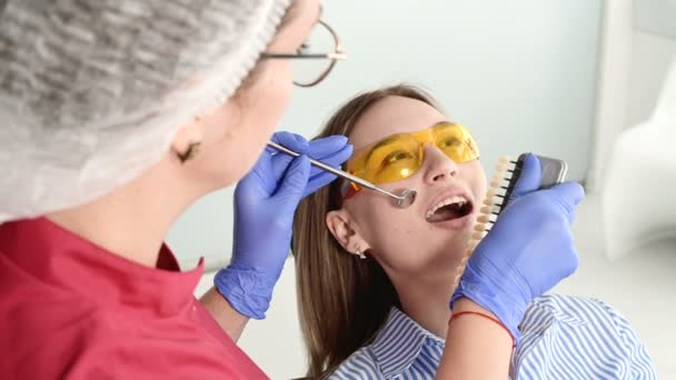 Die hübsche Blondine mit der gelben Schutzbrille auf dem Kopf untersuchte ihren offenen Mund. Zahnärztin untersucht Mundhöhle einer jungen Patientin mit Hilfe eines zahnärztlichen Instruments — Stockvideo