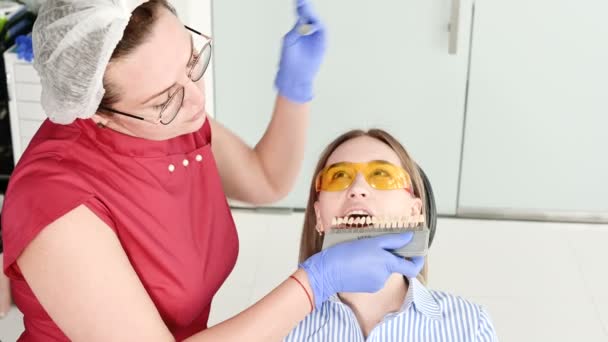 Pretty blonde girl in protective yellow glasses on the stamotologist examined her open mouth. Female dentist examines the oral cavity of a young patient with the help of a dentist instrument — Stock Video
