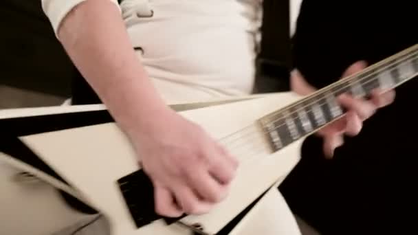 Közeli stílusos szólógitáros a raszta a fején és fehér ruhában a fekete háttér kifejezően játszik a fehér gitár egy fekete stúdióban — Stock videók