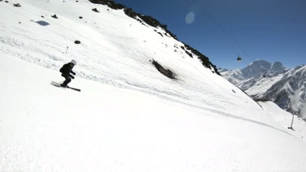 En vidvinkel manliga skidåkare åldrad i svart utrustning och vit hjälm med skidstavar rider på en snöig sluttning på en solig dag. Begreppet vinter skidsport — Stockvideo