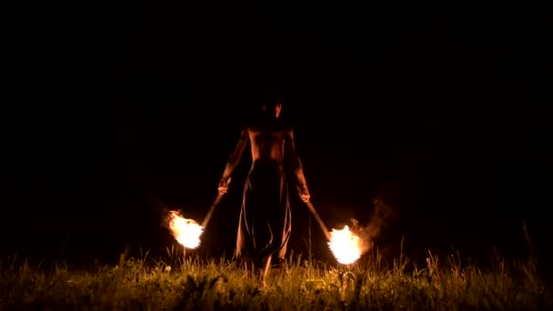 Low key. Young male with long hair and bare torso rotates burning torch outdoors on a black night video slow motion. Modern fakir does tricks with a burning staff — Stock Video