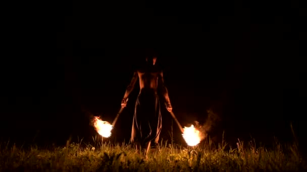 Très discret. Jeune homme aux cheveux longs et au torse nu tourne torche brûlante à l'extérieur sur une vidéo de nuit noire au ralenti. Fakir moderne fait des tours avec un bâton brûlant 