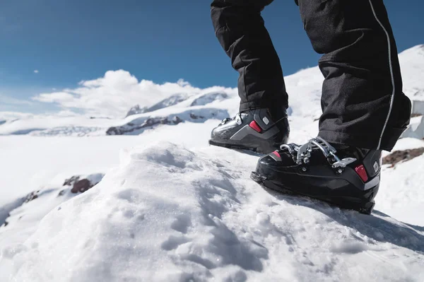 Un primo piano di una gamba di sciatori in scarponi da sci senza sci si erge su una collina di beatitudine sullo sfondo delle montagne in una giornata di sole. Il concetto di skittura e trekking ski travel — Foto Stock