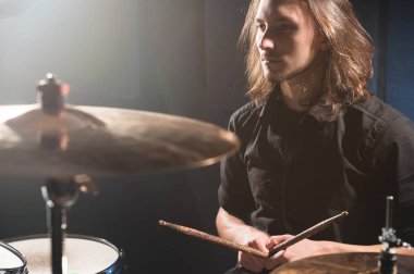Ellerini bir davul seti arkasında oturan Chopsticks ile uzun saçlı bir davulcu portresi. Düşük anahtar. Milenyal nesil yaratıcı özgürlüğü kavramları