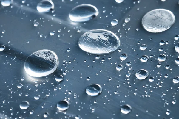 Close-up de gotas de chuva de diferentes tamanhos na superfície coberta com filme aderente. Tempo de umidade e conceito de umidade — Fotografia de Stock
