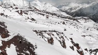 Kış sezonunda Elbrus beldesinde Kafkasya'nın yüksek dağlarında teleferik ve kayak pistlerinin havadan görünümü. Kabinlerin kablo yolunu izleme