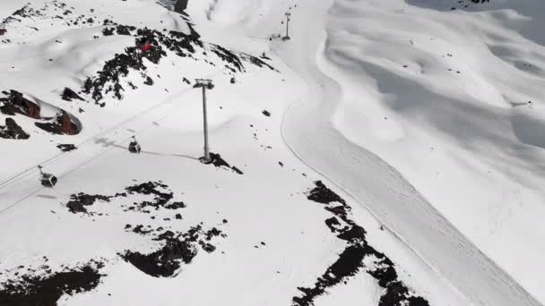 Vista aérea del teleférico y pistas de esquí en las altas montañas del Cáucaso en la estación de Elbrus en la temporada de invierno. Cabinas de seguimiento teleférico — Vídeo de stock