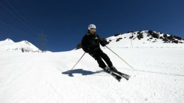 Siyah ekipman ve kayak direkleri ile beyaz kask yaşlı geniş açılı erkek kayakçı güneşli bir günde karlı bir yamaç üzerinde sürmek. Kış kayak sporları kavramı