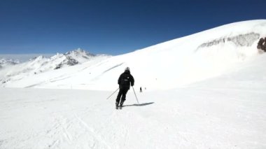 Siyah ekipman ve kayak direkleri ile beyaz kask yaşlı geniş açılı erkek kayakçı güneşli bir günde karlı bir yamaç üzerinde sürmek. Kış kayak sporları kavramı
