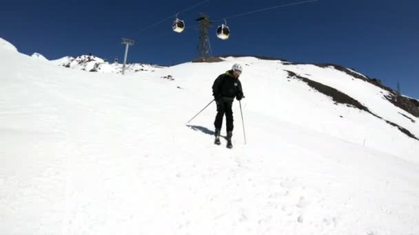 En vidvinkel manliga skidåkare åldrad i svart utrustning och vit hjälm med skidstavar rider på en snöig sluttning på en solig dag. Begreppet vinter skidsport — Stockvideo