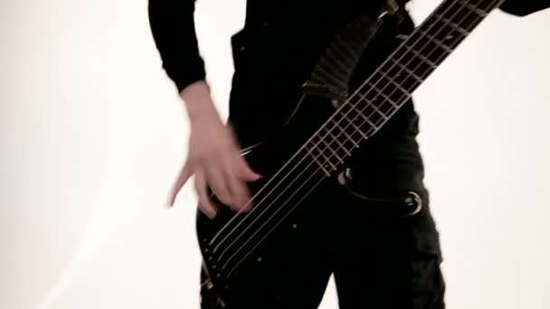 Joven músico masculino en ropa negra con un bajo negro sobre un fondo blanco. Bajo guitarrista expresivo juego de música — Vídeos de Stock