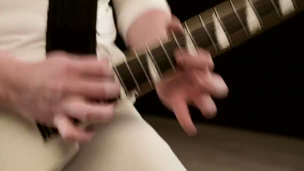 Close-up Elegante guitarrista solista con rastas en la cabeza y con ropa blanca sobre un fondo negro tocando la guitarra blanca en un estudio negro — Vídeo de stock