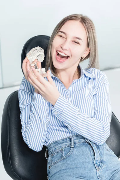 Porträtt av en lycklig attraktiv flicka i en tandläkarstol. Laughing Girl på tandläkare utnämningen med en käke modell i hennes händer — Stockfoto