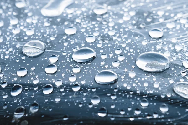 Close-up de gotas de chuva de diferentes tamanhos na superfície coberta com filme aderente. Tempo de umidade e conceito de umidade — Fotografia de Stock