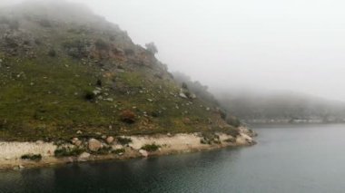 Kayalık bir sahilin havadan görünümü. Bulutlu hava ve sis tepeler arasında Dağ turkuaz göl. Kuzey Kafkasya Manzaraları