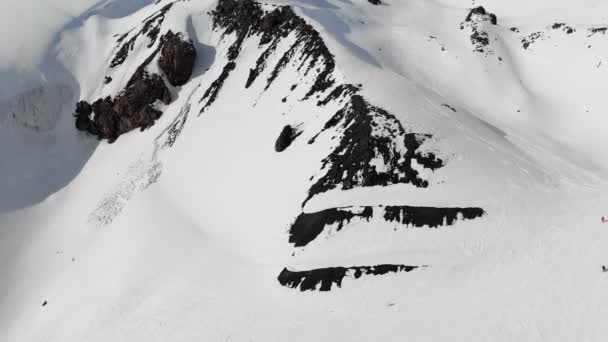 Veduta aerea di un paesaggio montano invernale. I pendii rocciosi innevati della località dell'Elbrus meridionale con piste da sci sulla neve. Concetto sport invernali — Video Stock