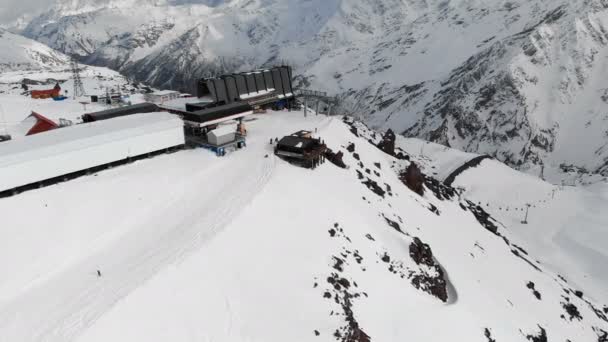 Σταθμός εναέριας προβολής ενός λιφτ του σκι με καμπίνες ψηλά στα βουνά του Καυκάσου στο θέρετρο του Elbrus κατά τη χειμερινή περίοδο. Επισκόπηση σταθμού και συρματόσχοινα — Αρχείο Βίντεο