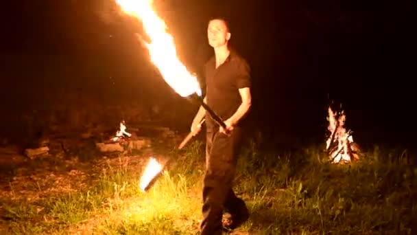 Très discret. Jeune homme aux cheveux longs tourne torche brûlante à l'extérieur sur une vidéo de nuit noire au ralenti. Fakir moderne fait des tours avec un bâton brûlant — Video