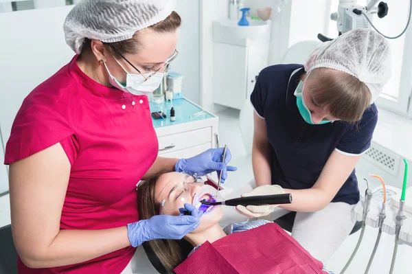 Γυναίκα οδοντίατρος και νοσοκόμα κάνοντας ένα νέο UV αποξηραμένο νεαρό ασθενή πλήρωση στο οδοντιατρείο — Φωτογραφία Αρχείου