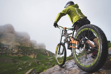 Bir dağ bisikleti üzerinde bir adamın arka görüş geniş açı kayalık bir arazi üzerinde duruyor ve bir kaya bakar. Bir dağ bisikleti ve mtb yokuş aşağı kavramı