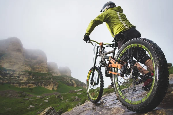 Vista trasera gran angular de un hombre en una bicicleta de montaña se encuentra en un terreno rocoso y mira a una roca. El concepto de una bicicleta de montaña y mtb cuesta abajo —  Fotos de Stock