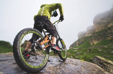 Bir dağ bisikleti üzerinde bir adamın arka görüş geniş açı kayalık bir arazi üzerinde duruyor ve bir kaya bakar. Bir dağ bisikleti ve mtb yokuş aşağı kavramı