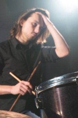 Elinde çubuklarla defokus lanmış uzun saçlı bir davulcunun davul setinin arkasında oturan portresi. Düşük anahtar. Bin yıllık neslin yaratıcı özgürlüğü kavramları