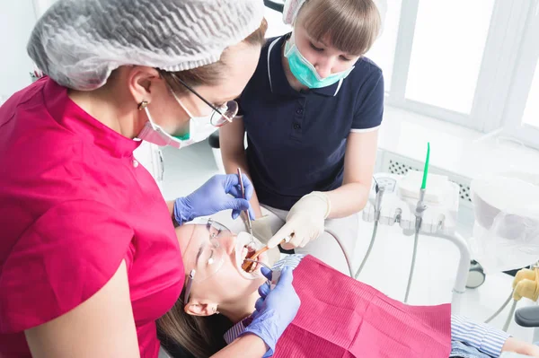 Γυναίκα οδοντίατρος και νοσοκόμα κάνει επαγγελματική φροντίδα και οδοντικό βούρτσισμα ενός νεαρού ασθενούς σε ένα οδοντιατρείο — Φωτογραφία Αρχείου
