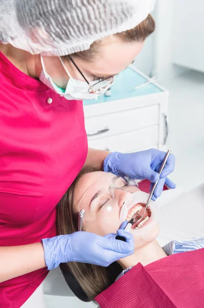 Close-up de um dentista aplicando polímero de uma seringa para o interior de um dente dianteiro de pacientes jovens em um consultório odontológico — Fotografia de Stock