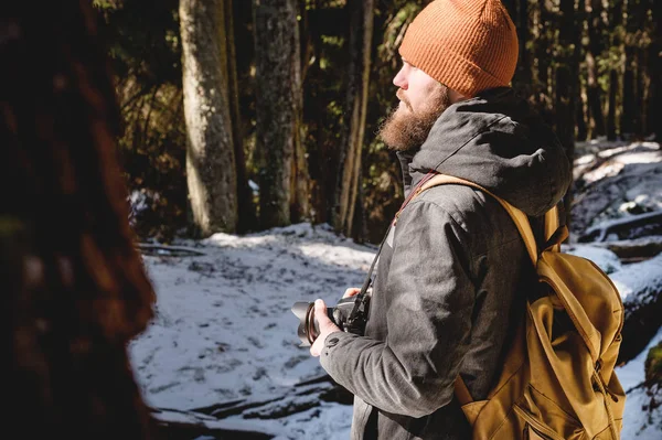 Πορτρέτο ενός μουσάτη φωτογράφο με μια αντανακλαστική κάμερα στα χέρια του στο χειμερινό δάσος κωνοφόρων. Φωτογραφία ταξίδι ιδέα — Φωτογραφία Αρχείου