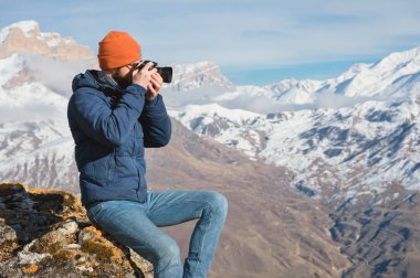 Güneş gözlüğü ve bir kap sakallı bir gezgin fotoğrafçı portresi dağların arka planında elinde ayna kamera ile bir kaya üzerinde oturur