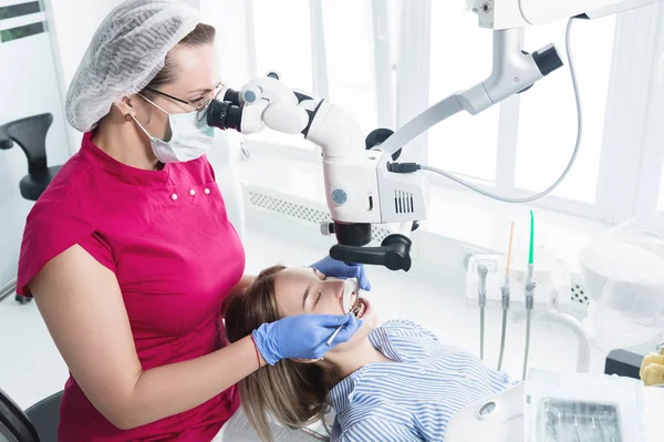 女性専門の歯科医が、彼女のオフィスで立体顕微鏡で女性患者を診察します。スタモトロジスト職業概念 — ストック写真