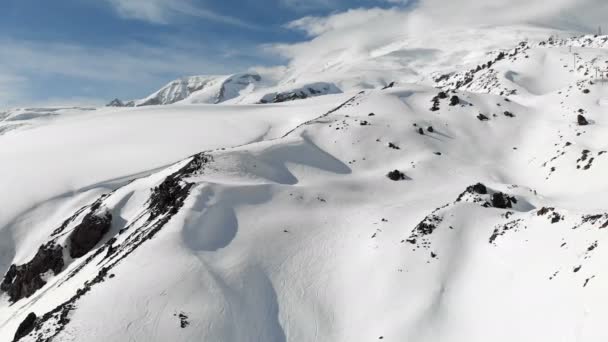 Widok z lotu ptaka na zimowy krajobraz górski. Pokryte śniegiem skaliste zbocza kurortu południowego regionu Elbrus z trasami narciarskimi na śniegu. Koncepcja sportów zimowych — Wideo stockowe