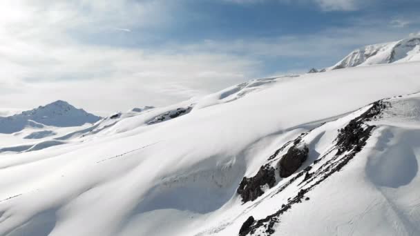 Vista aérea de uma paisagem de montanha de inverno. As encostas rochosas cobertas de neve do resort da região sul de Elbrus com pistas de esqui na neve. Conceito de esportes de inverno — Vídeo de Stock