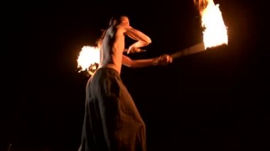 Düşük anahtar. Uzun saçlı ve çıplak gövde ile genç erkek siyah bir gece video yavaş hareket açık havada yanan meşale döner. Modern fakir bir yanan personel ile hileler yapar